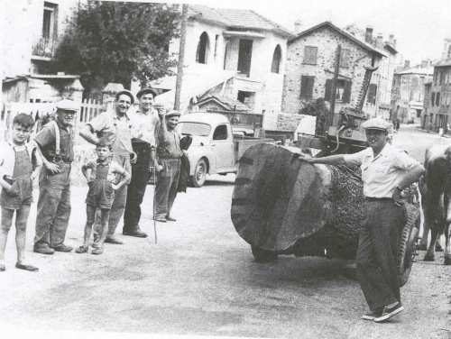 Des hommes autour d’une grosse grume dans la rue du village